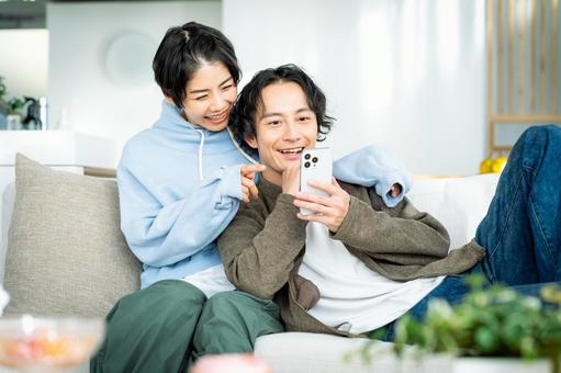 リビングでスマホを見る若い日本人カップル リビングでスマホを見る若い日本人カップルの写真